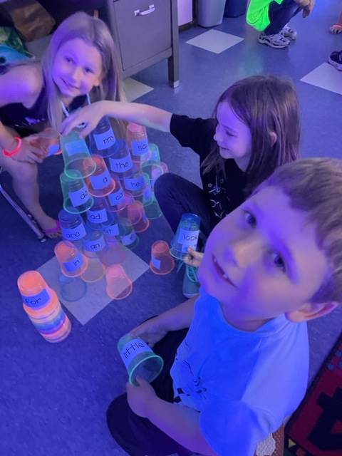 3 students building a fluorescent pyramid from plastic cups