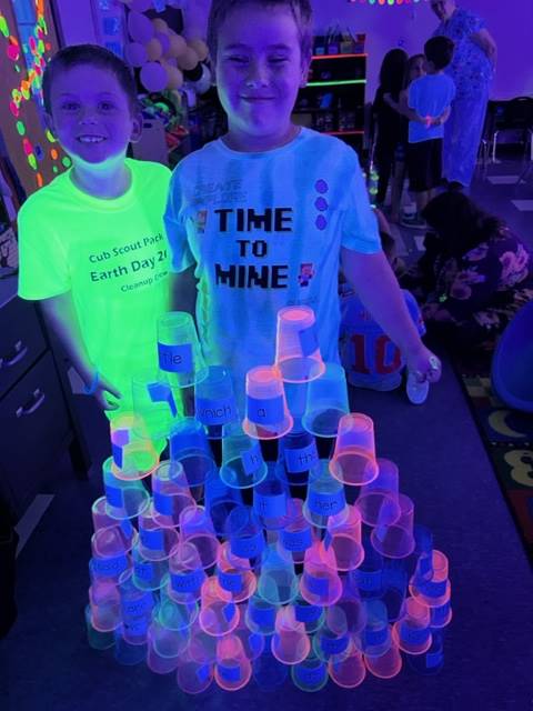 2 students proudly display a glowing cup pyramid