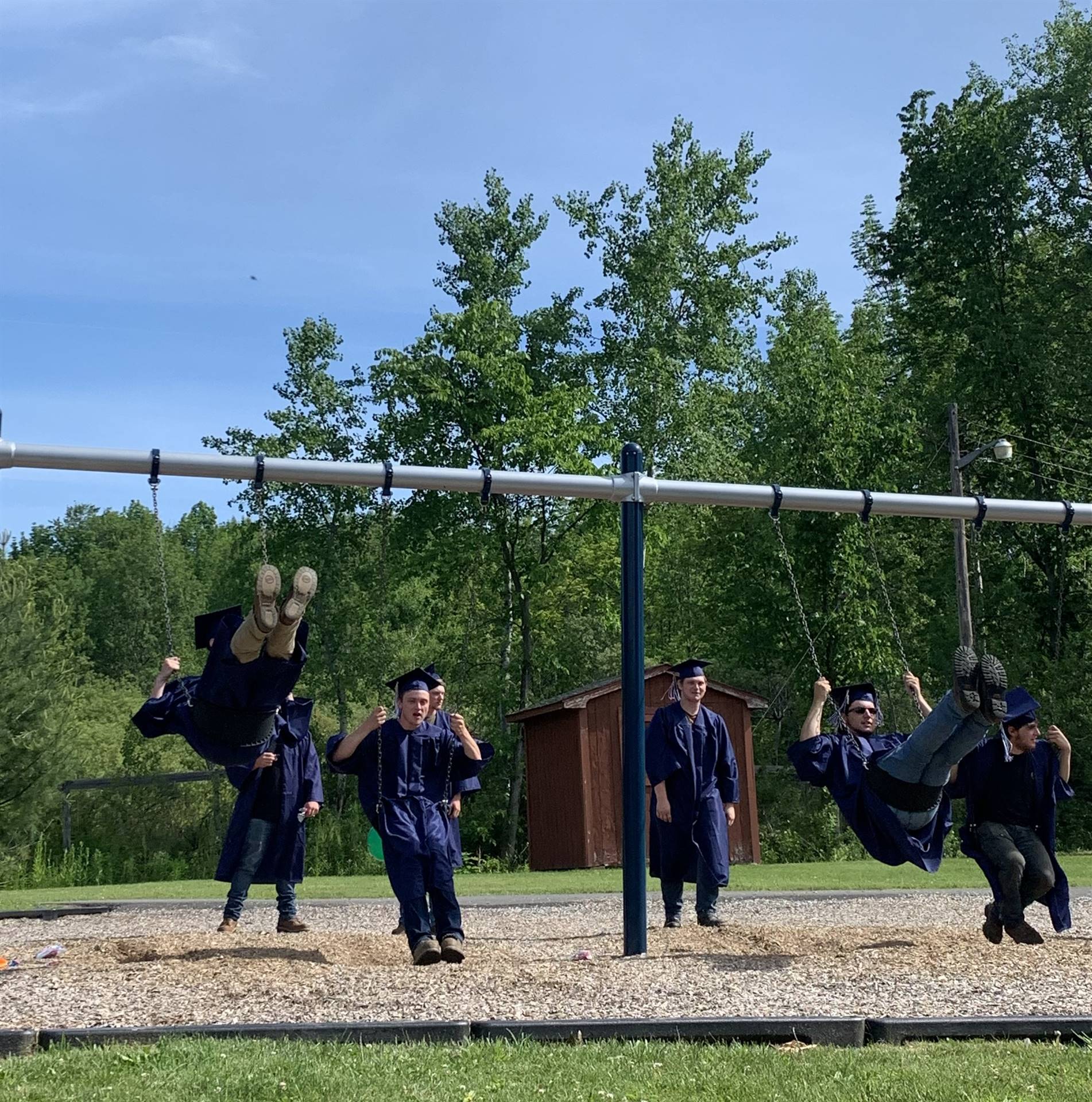 high school graduates in cap and gown swing on playground