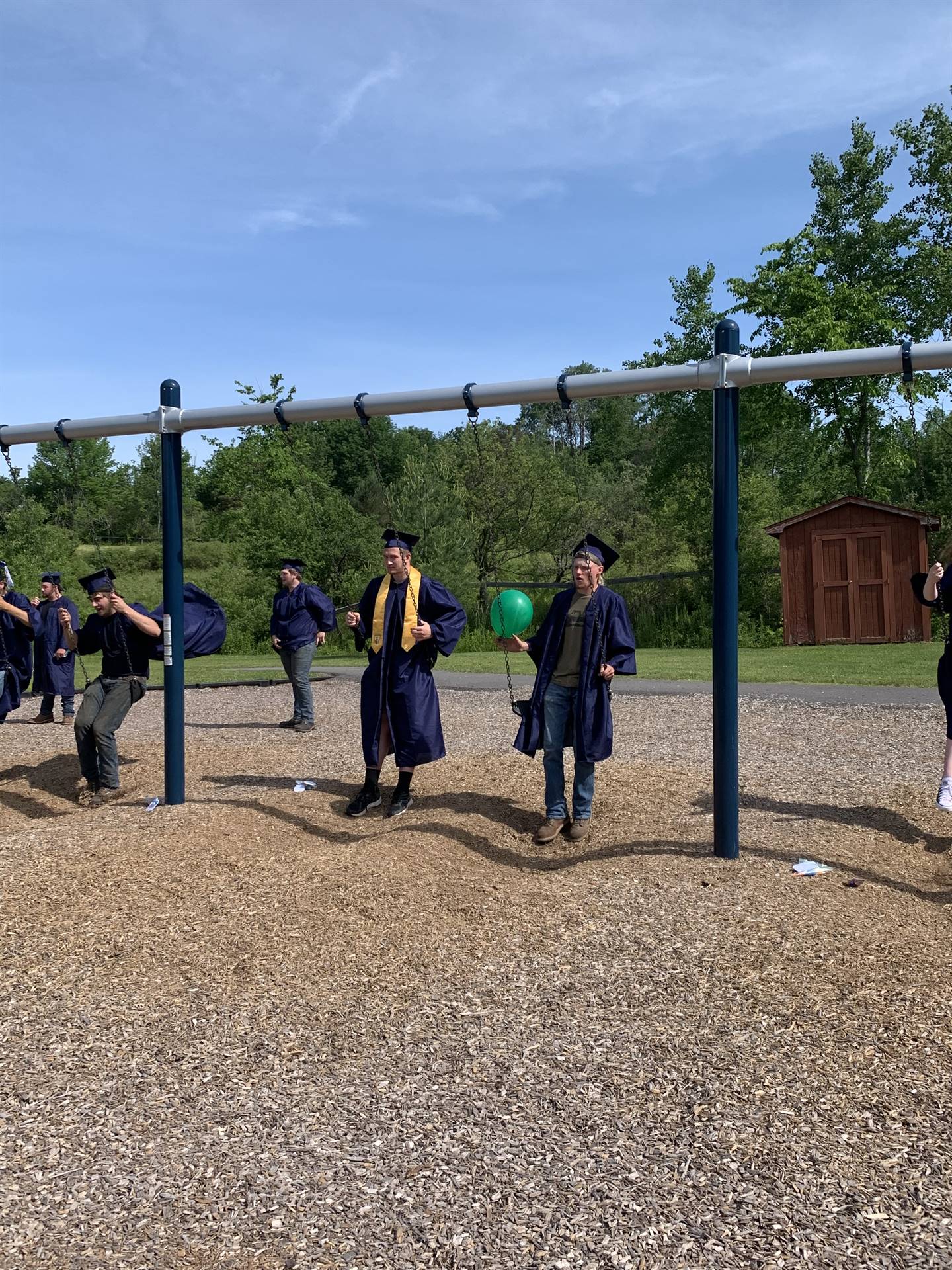high school graduates in cap and gown swing on playground