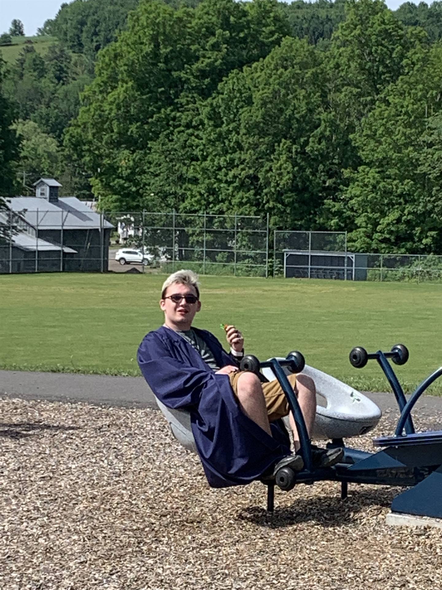 high school graduate sits on a playground ride.