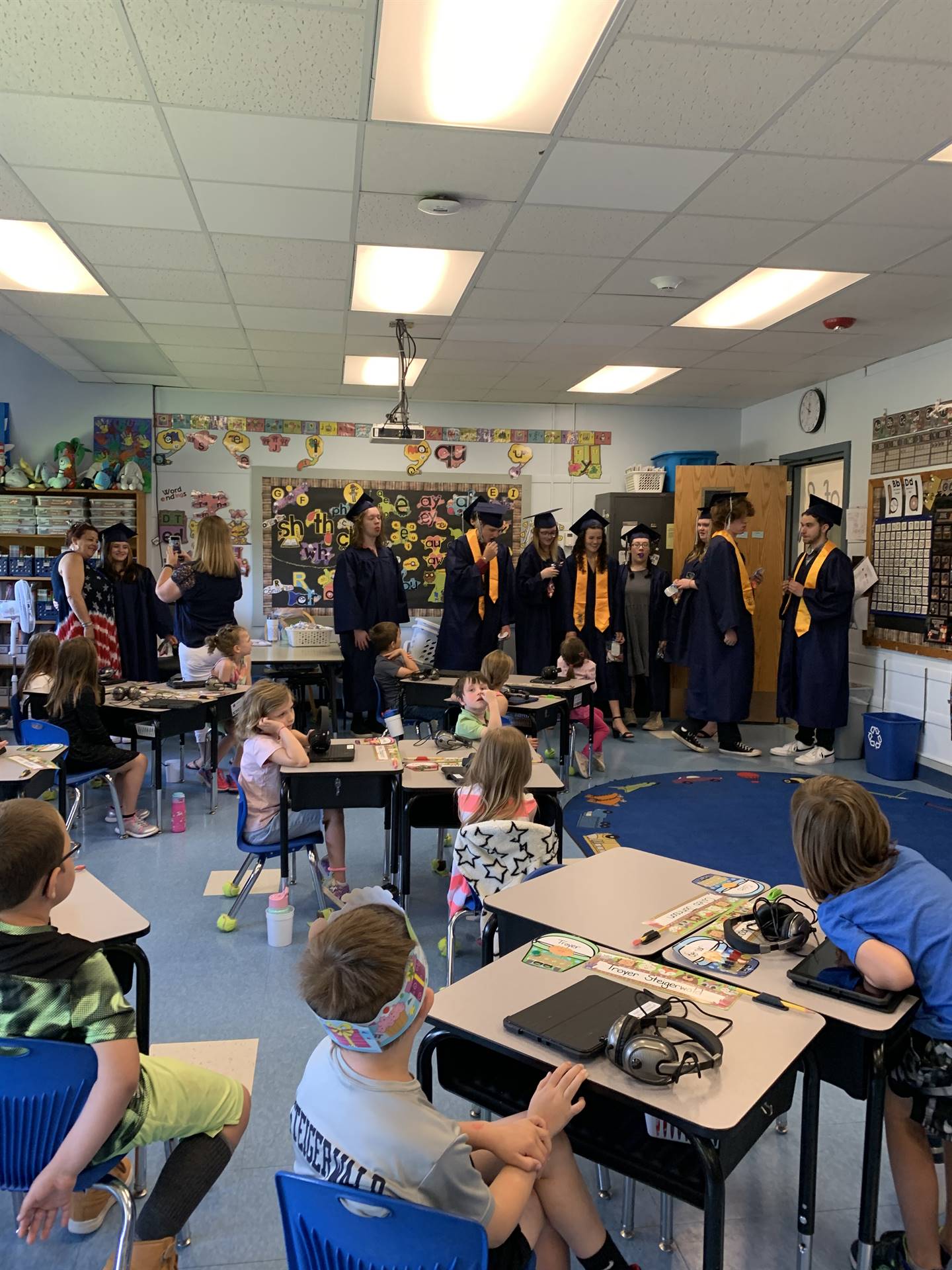 high school students in cap and gown pose with kindergarten students