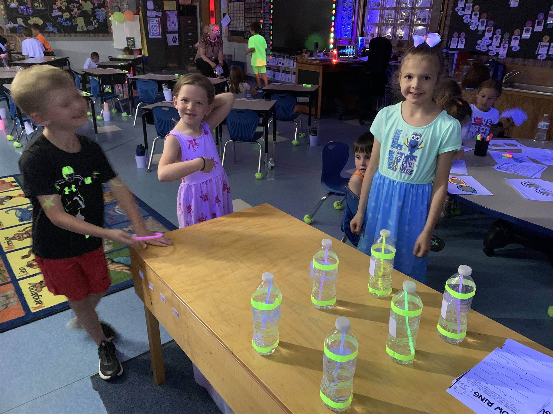 3 students playing a glow day game with bottles and straws.