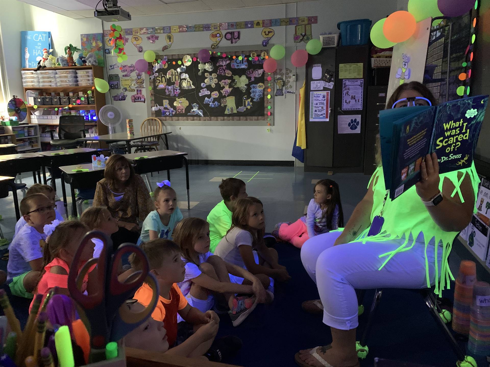 a class listens to a teacher read a story during a glow day.