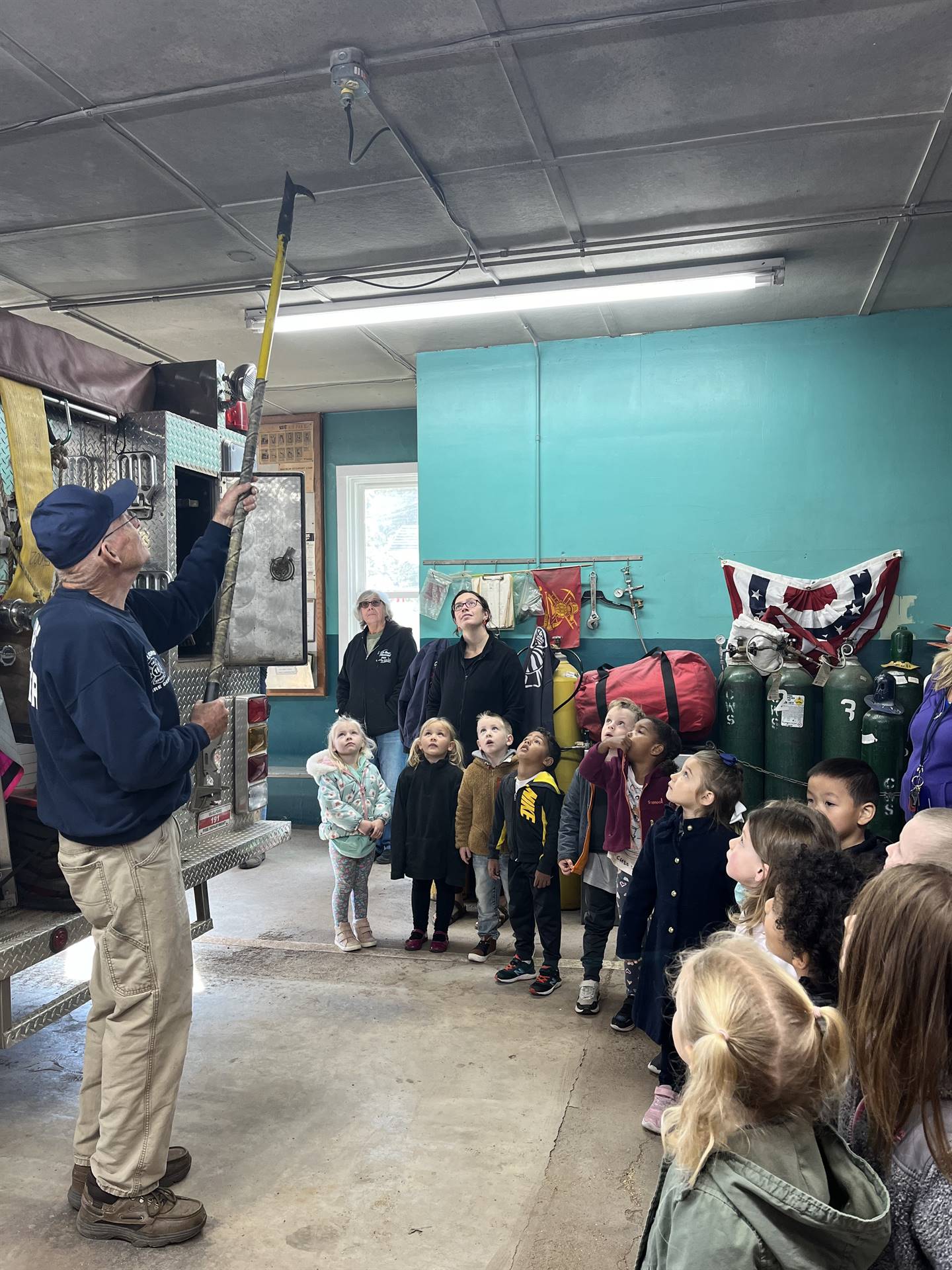 A firefighter demonstrates how they poke through ceilings to find fires to a group of students. 