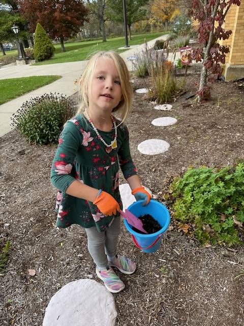 A student shoveling dirt in a pail in a garden outside.