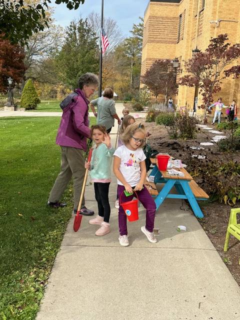 A group  of students and an adult with pails, diggers, and other garden materials outside.