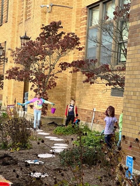 3 students pretending to be scarecrows in a garden outside.