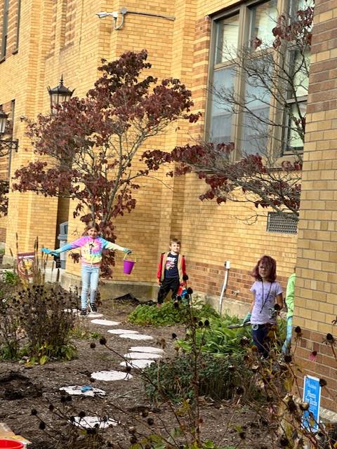 3 students pretending to be scarecrows in a garden outside.