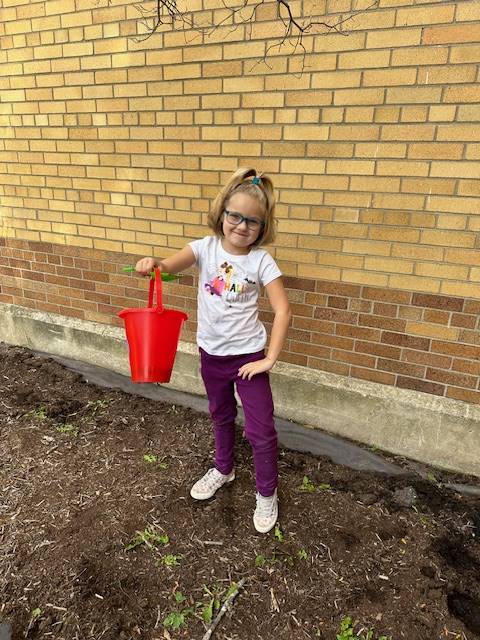 A student holding up a pail in a garden outside.