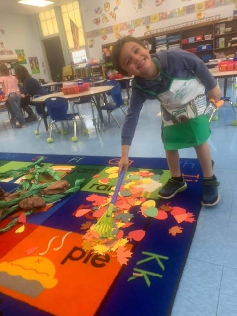 A student rakes paper leaves in a pumpkin themed center.