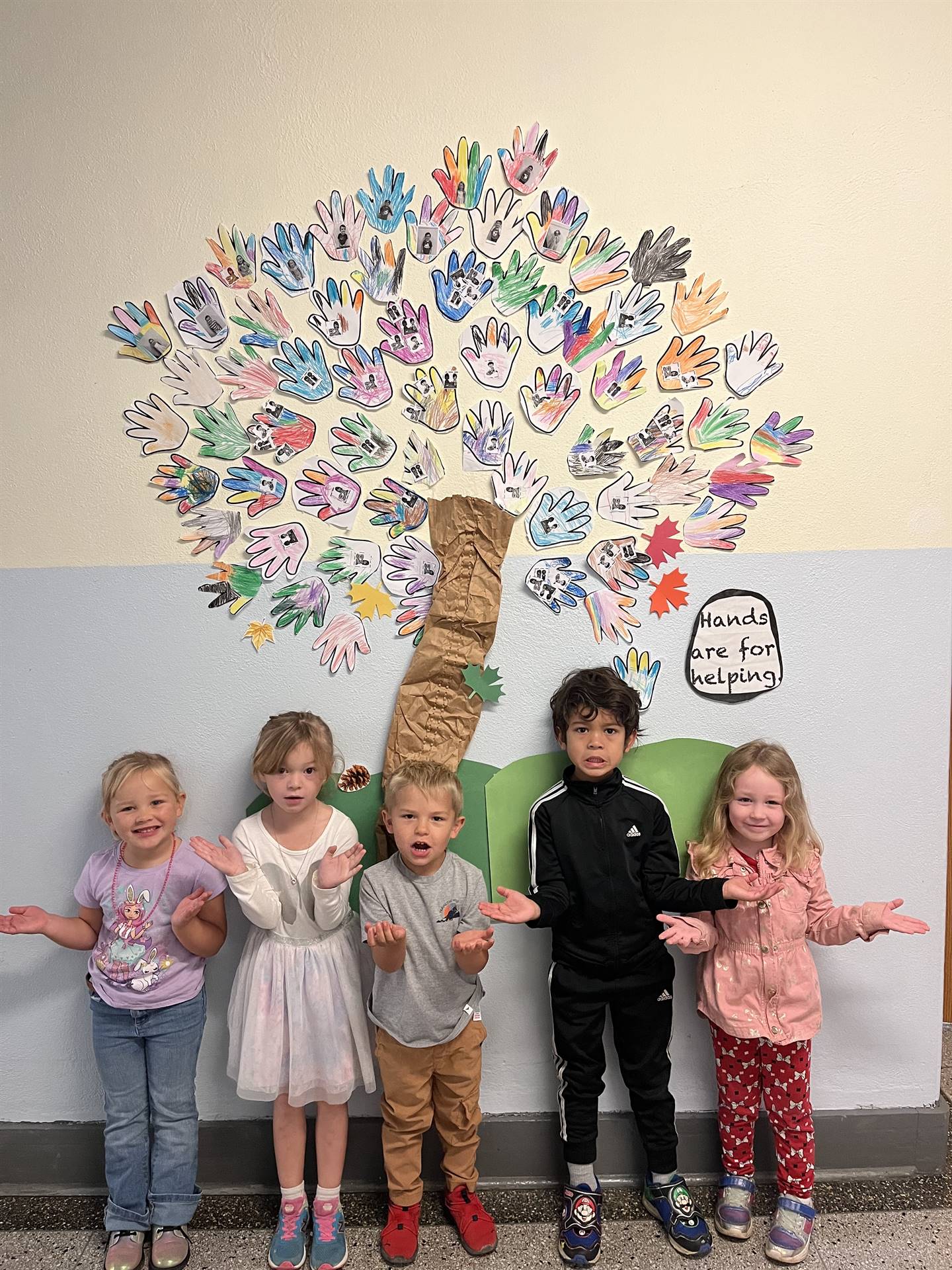students next to tree made out of paper hands.