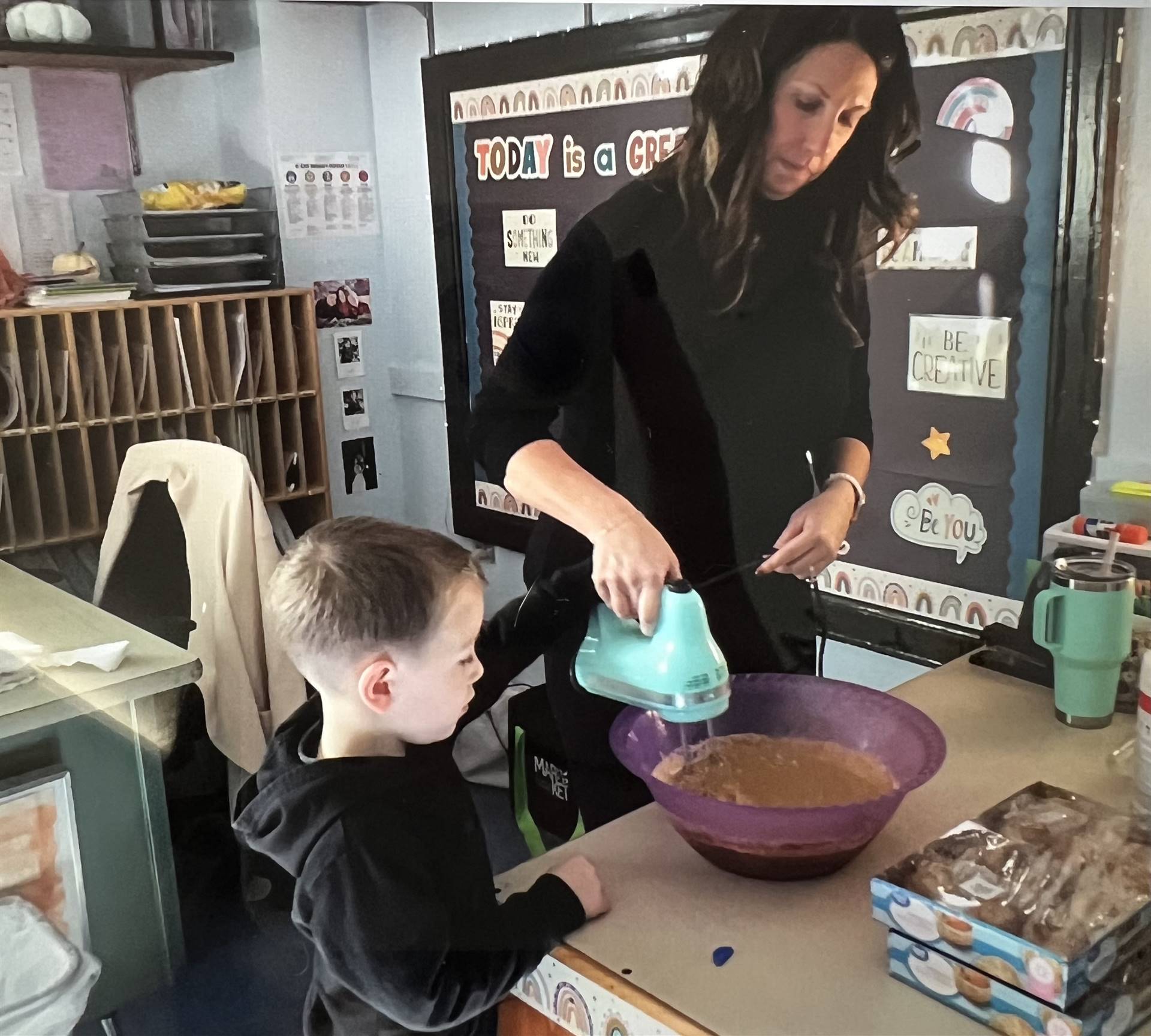 A teacher uses a mixer with a student to mix a batter.