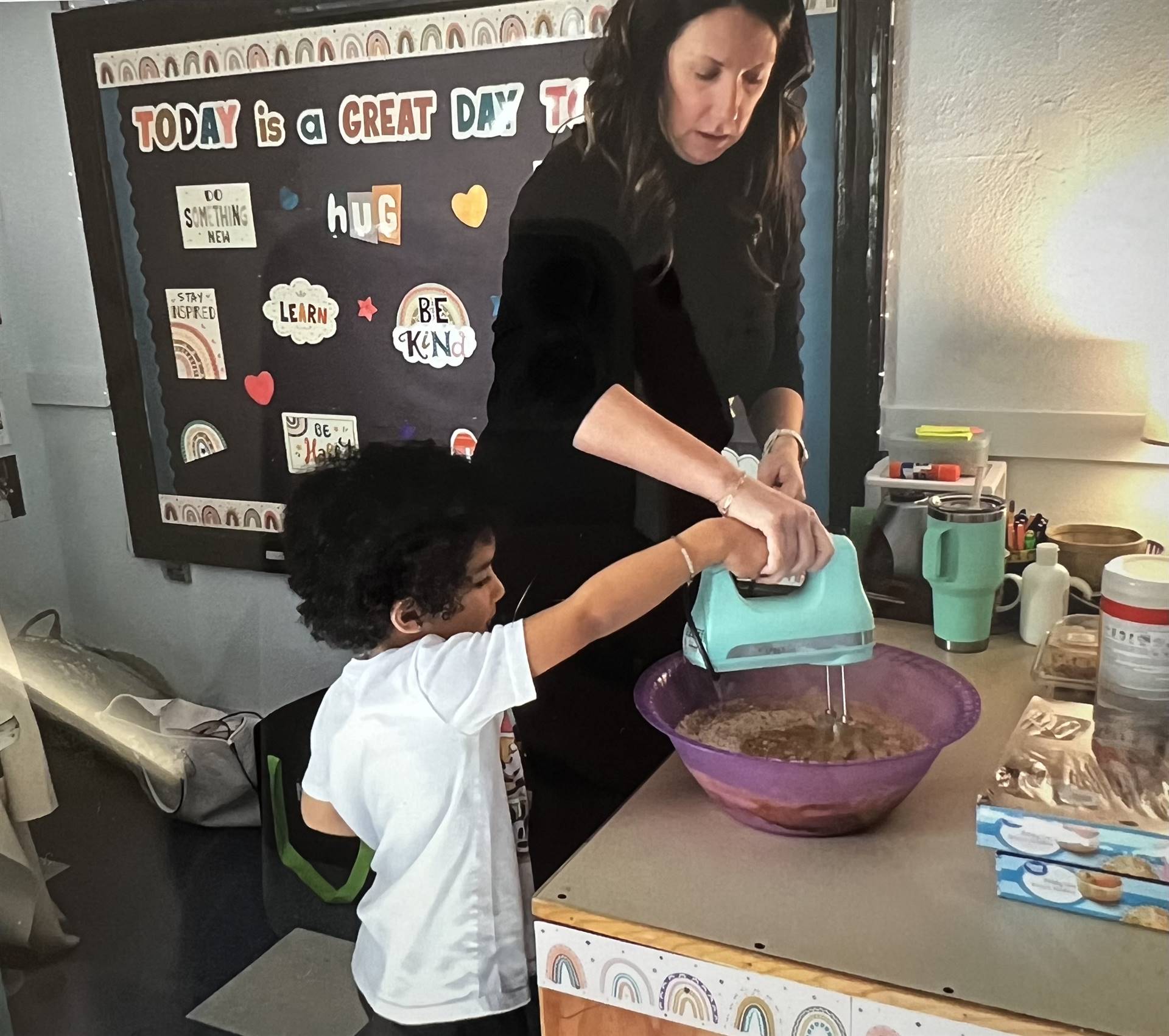 A teacher uses a mixer with a student to mix a batter.