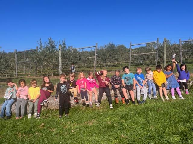 a student class sits on a rock with apple orchard behind them 