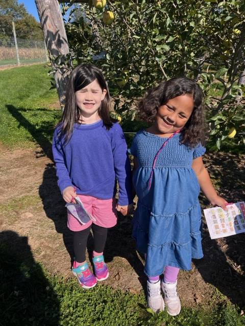 2 kids in apple orchard with apple trees behind them