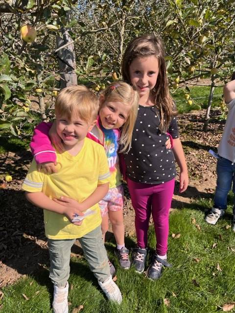 kids in apple orchard with apple trees behind them