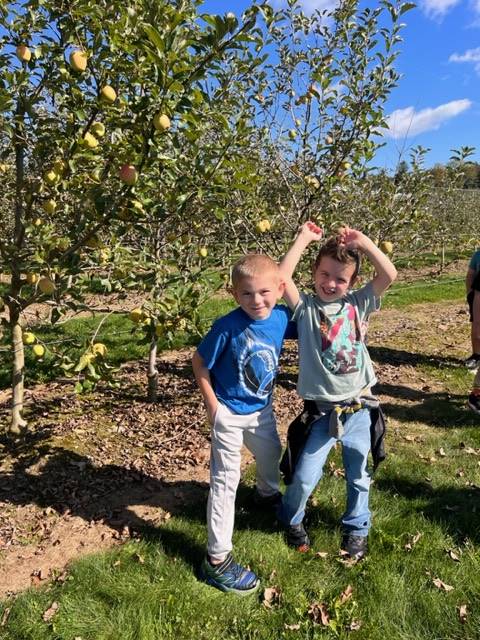 2 kids in apple orchard with apple trees behind them