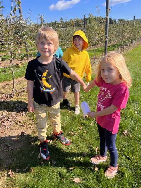  kids in apple orchard with apple trees behind them