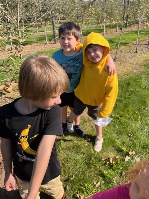  kids in apple orchard with apple trees behind them