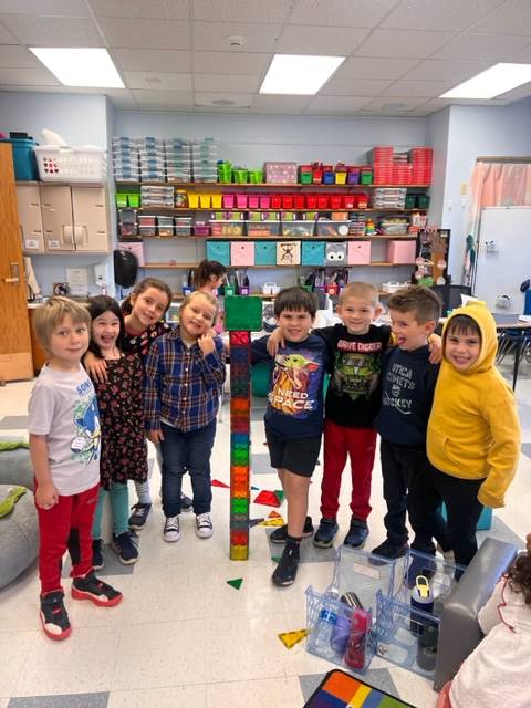 a group of student standing around a tall tower they built from colorful magna tiles