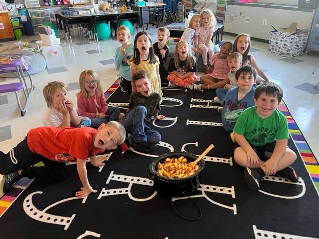 a group of students sit with a pot of cut apples in their middle.