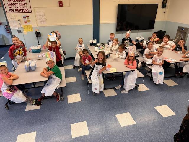 students sitting at tables with aprons and chef hats on.