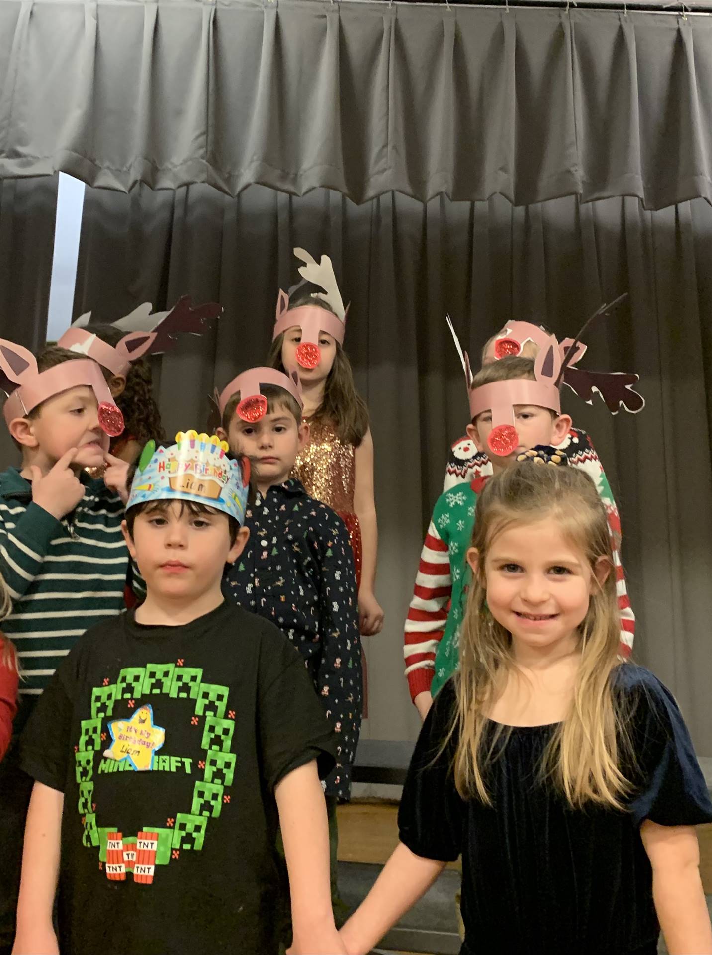 students wearing red noses and reindeer antlers sing on stage