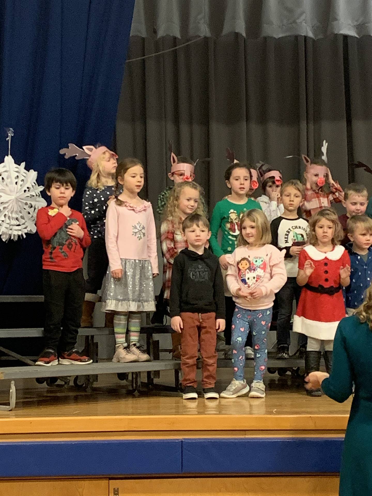 students wearing red noses and reindeer antlers sing on stage
