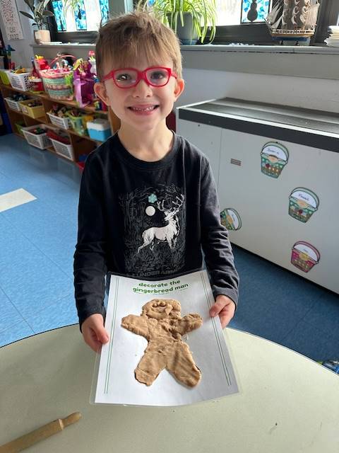 student holds up a play do  gingerbread friend.
