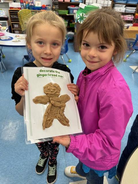 2 students hold up a play do  gingerbread friend they created together. 