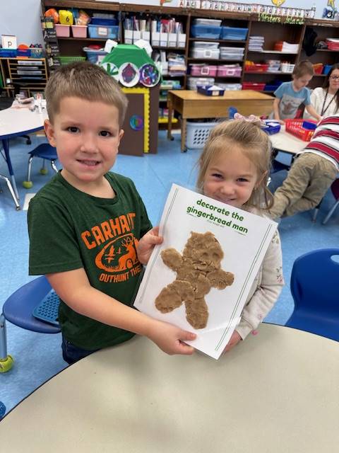 2 students hold up a play do  gingerbread friend they created together. 