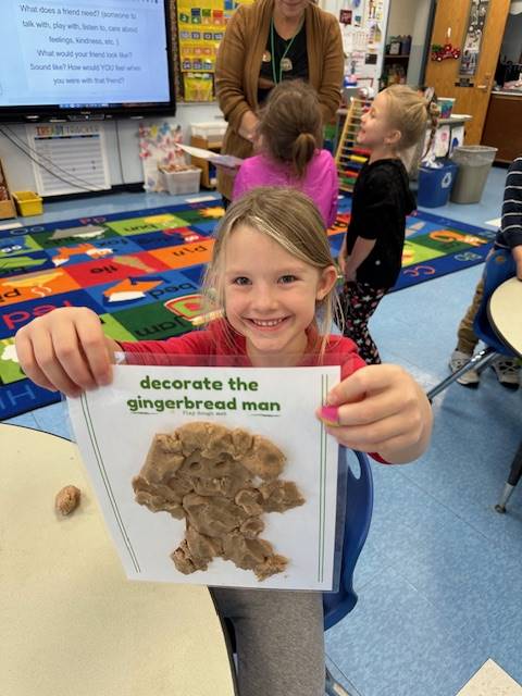 A student holds up a play do  gingerbread friend . 