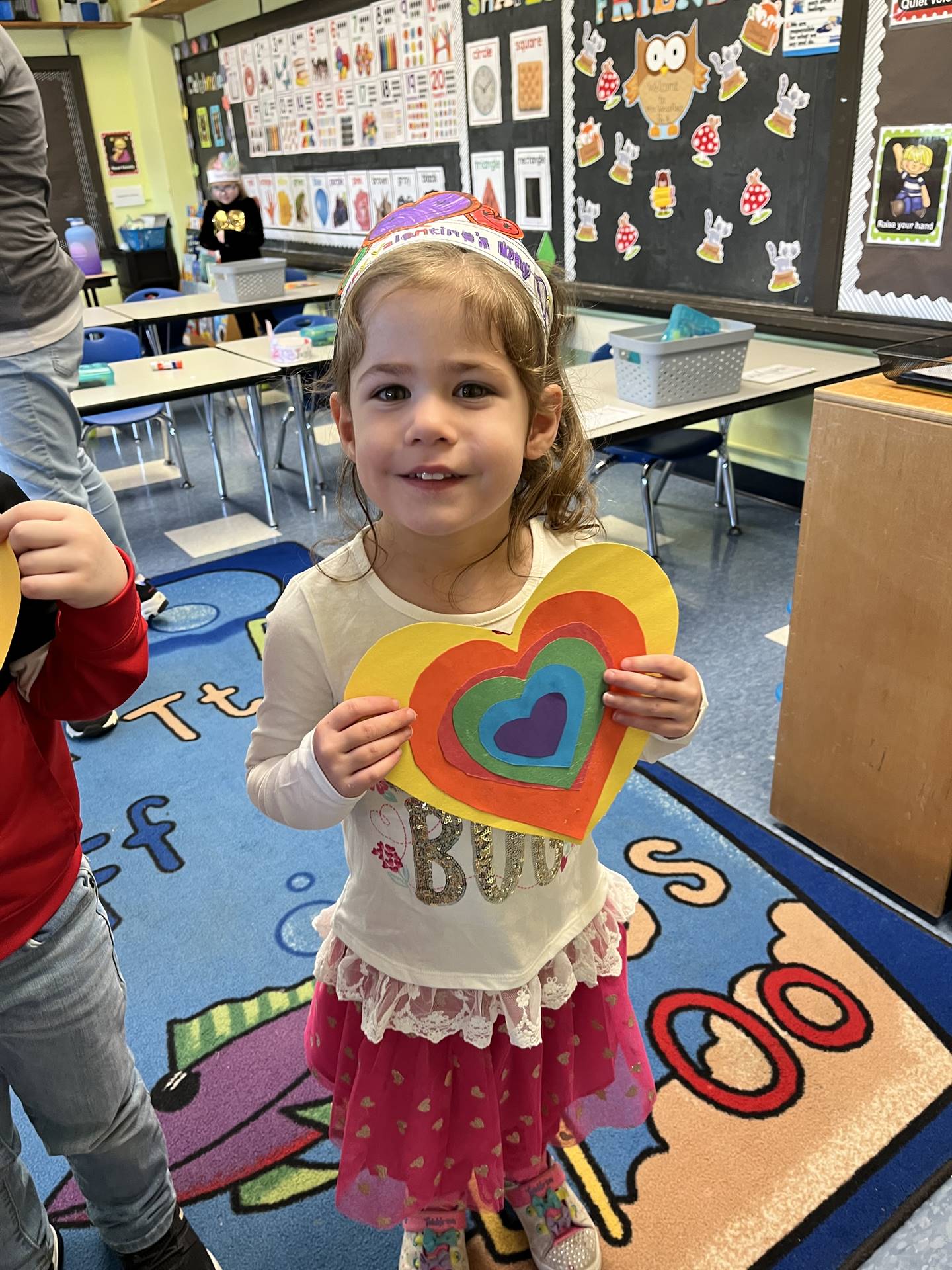 student holding a paper craft rainbow heart.