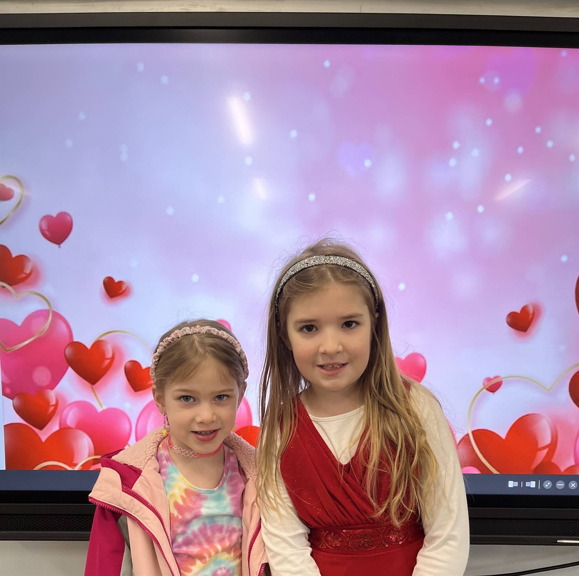 2 students dressed in red with heart background.