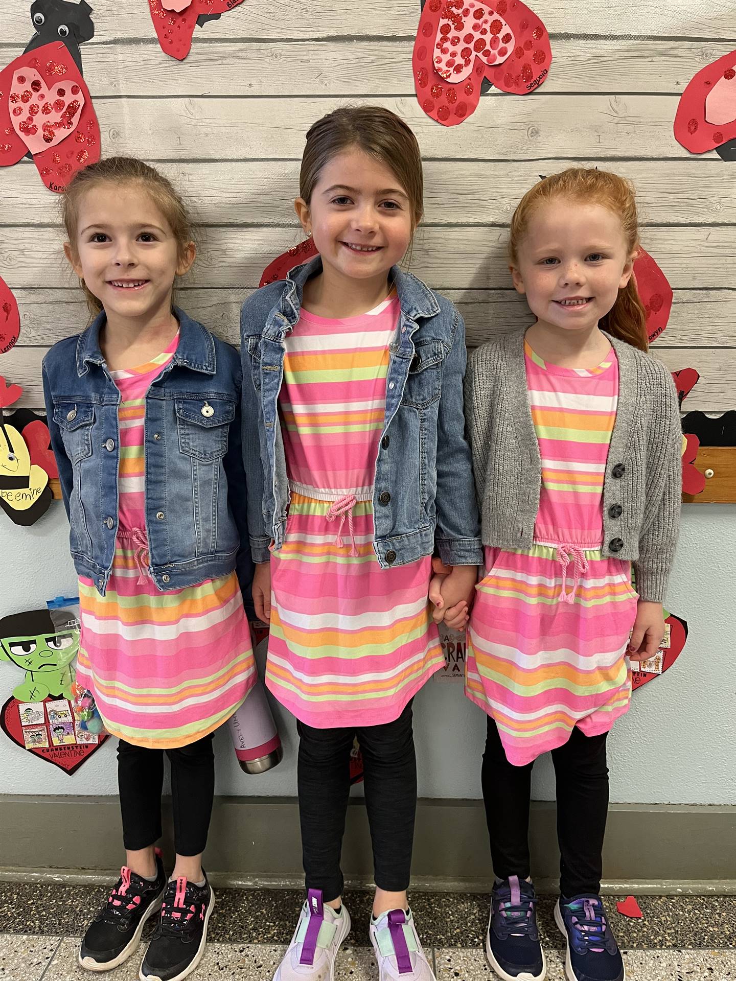 3 students dressed in pink and yellow striped shirts with heart background
