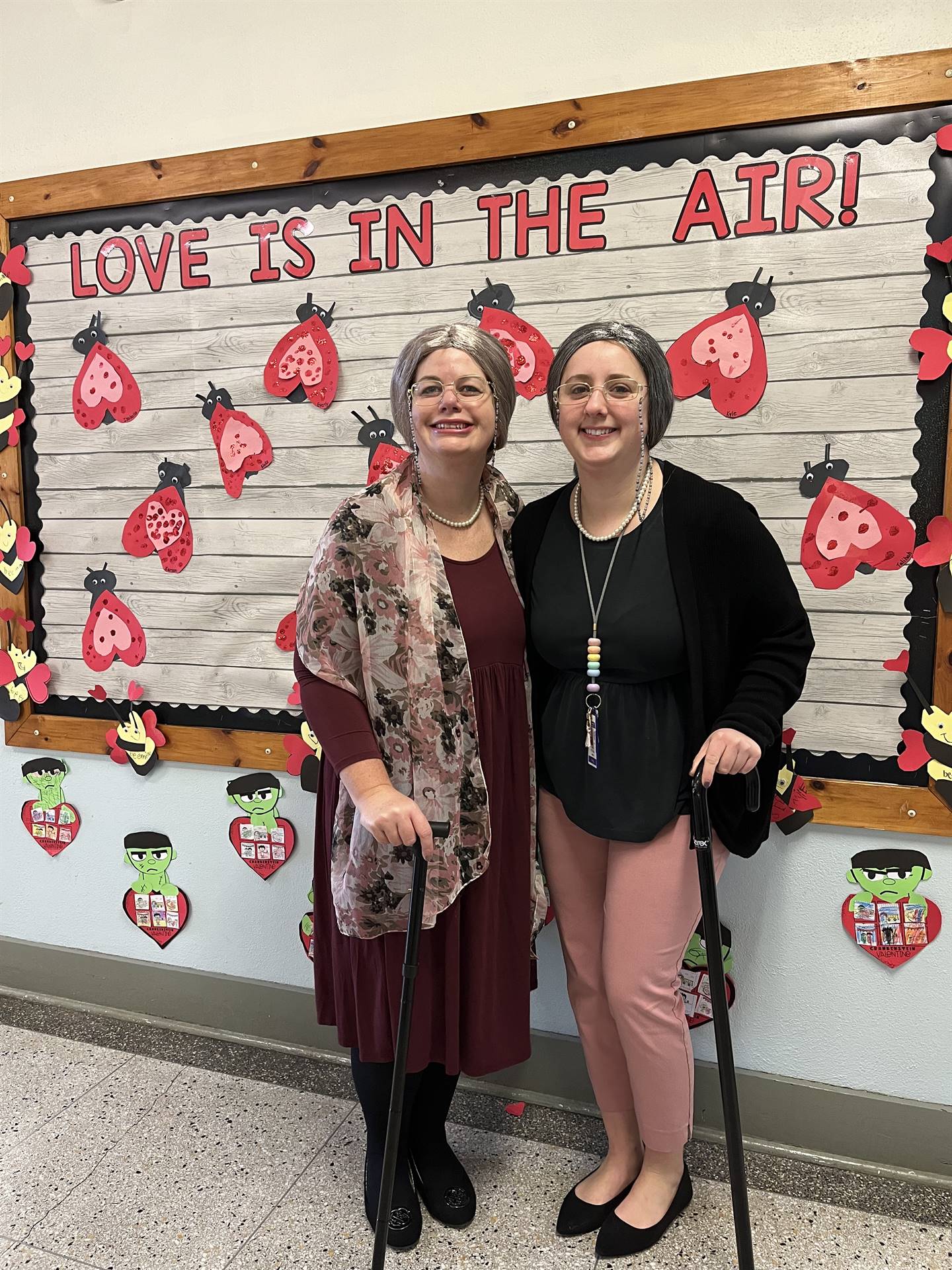 2 teachers dressed as 100 year olds complete with canes and a heart background