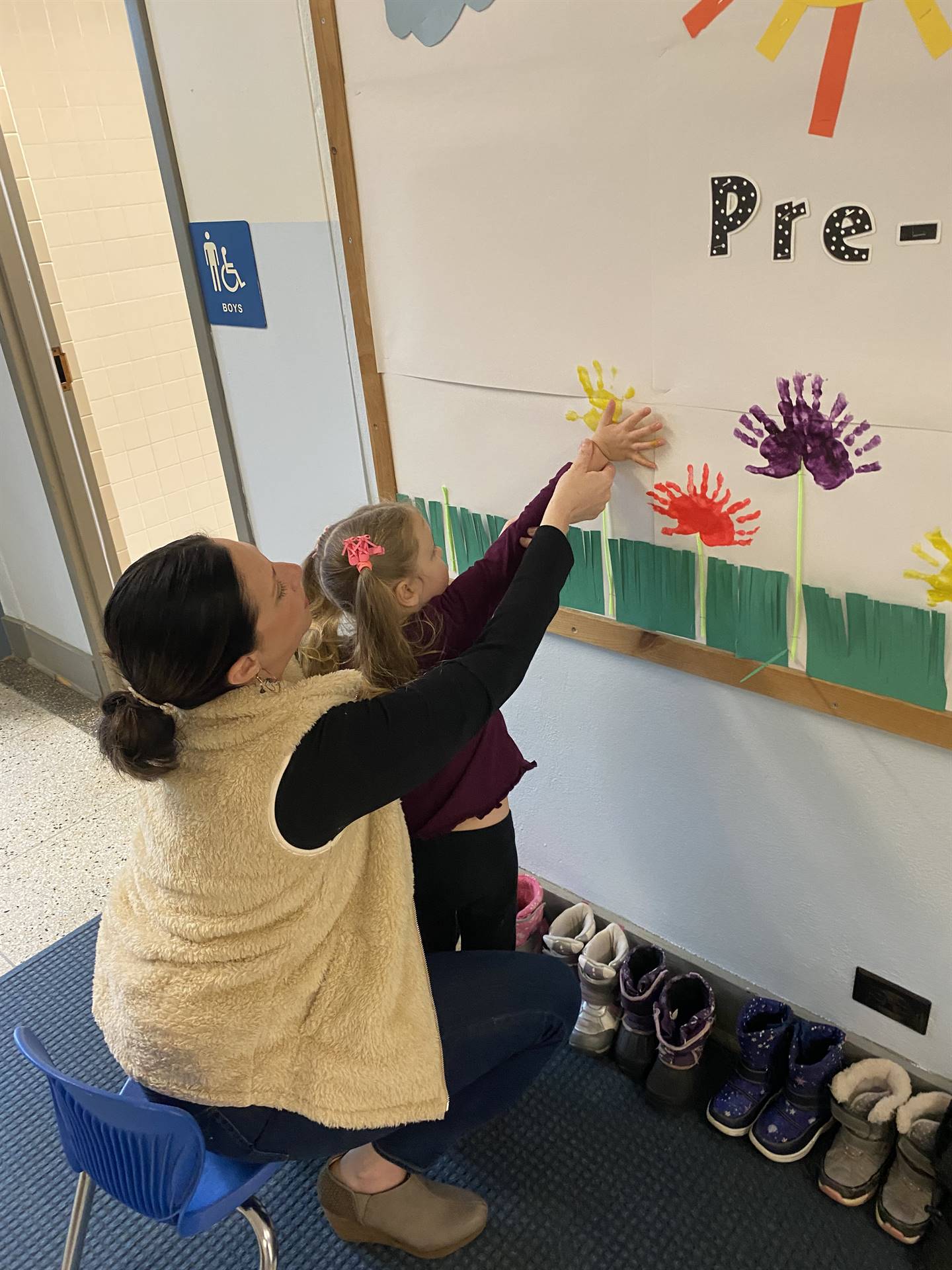 teacher holding student's painted hand onto bulletin board