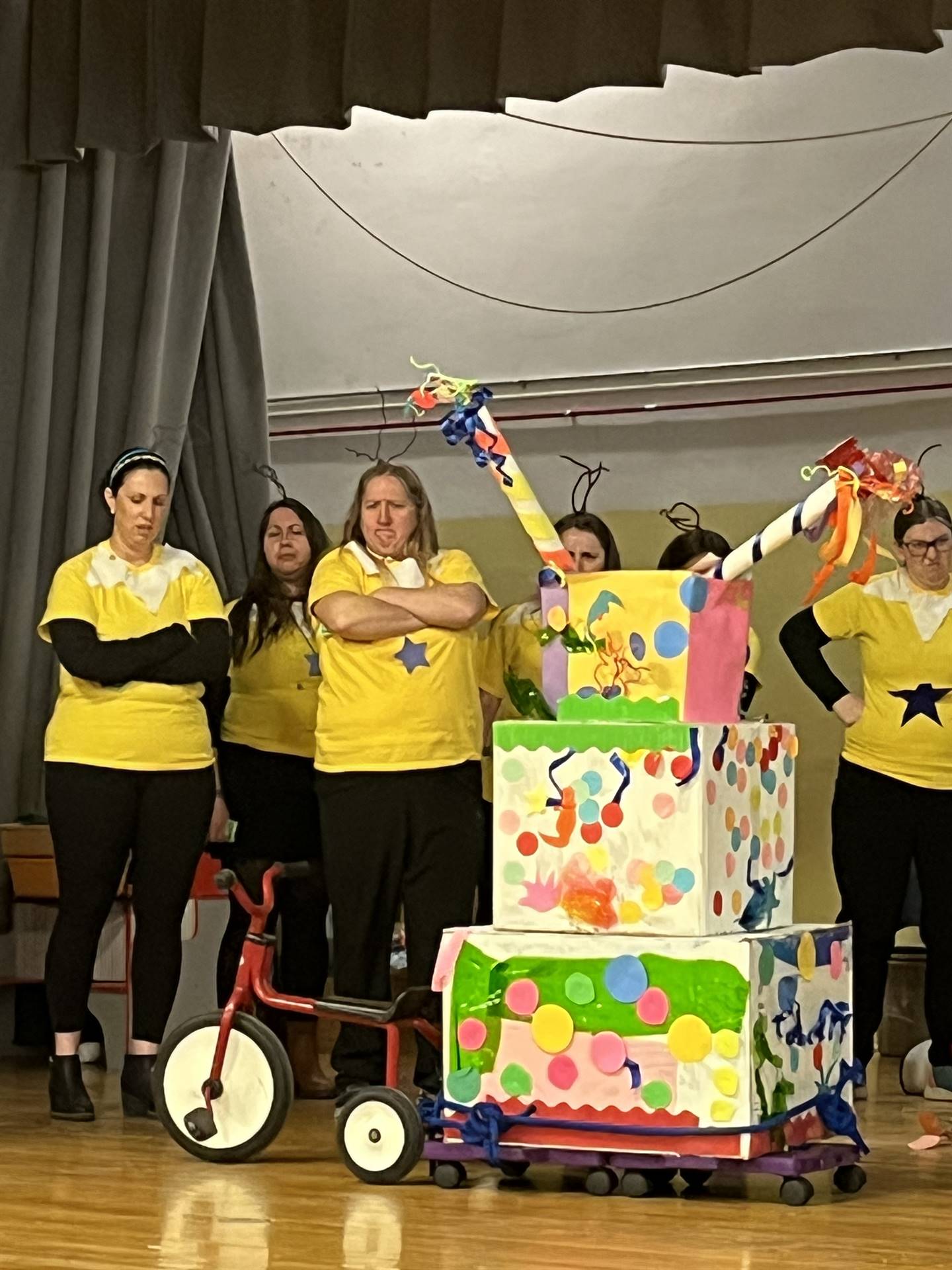 Teachers dressed in yellow shirts and arms crossed behind a brightly colored machine
