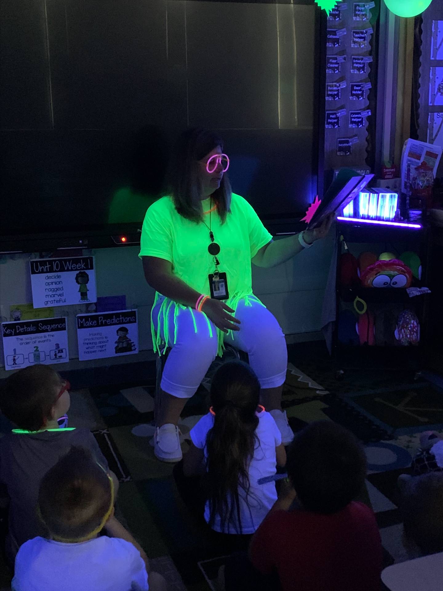 a teacher in a glowing neon shirt reads to her class