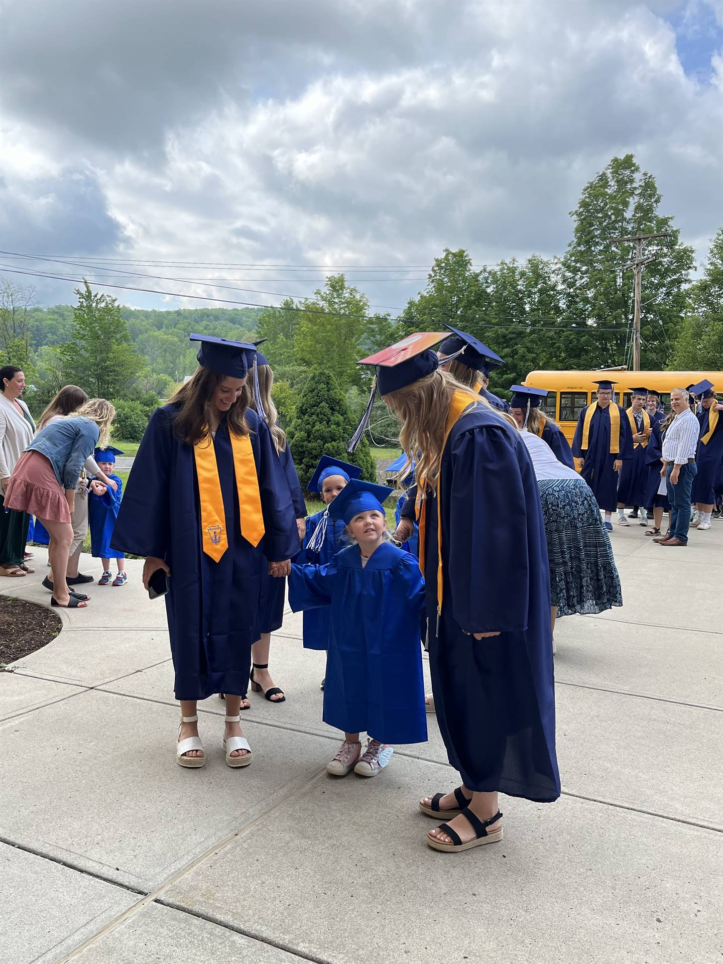 2 2023 senior graduates with a pre k student in middle dressed in caps and gowns