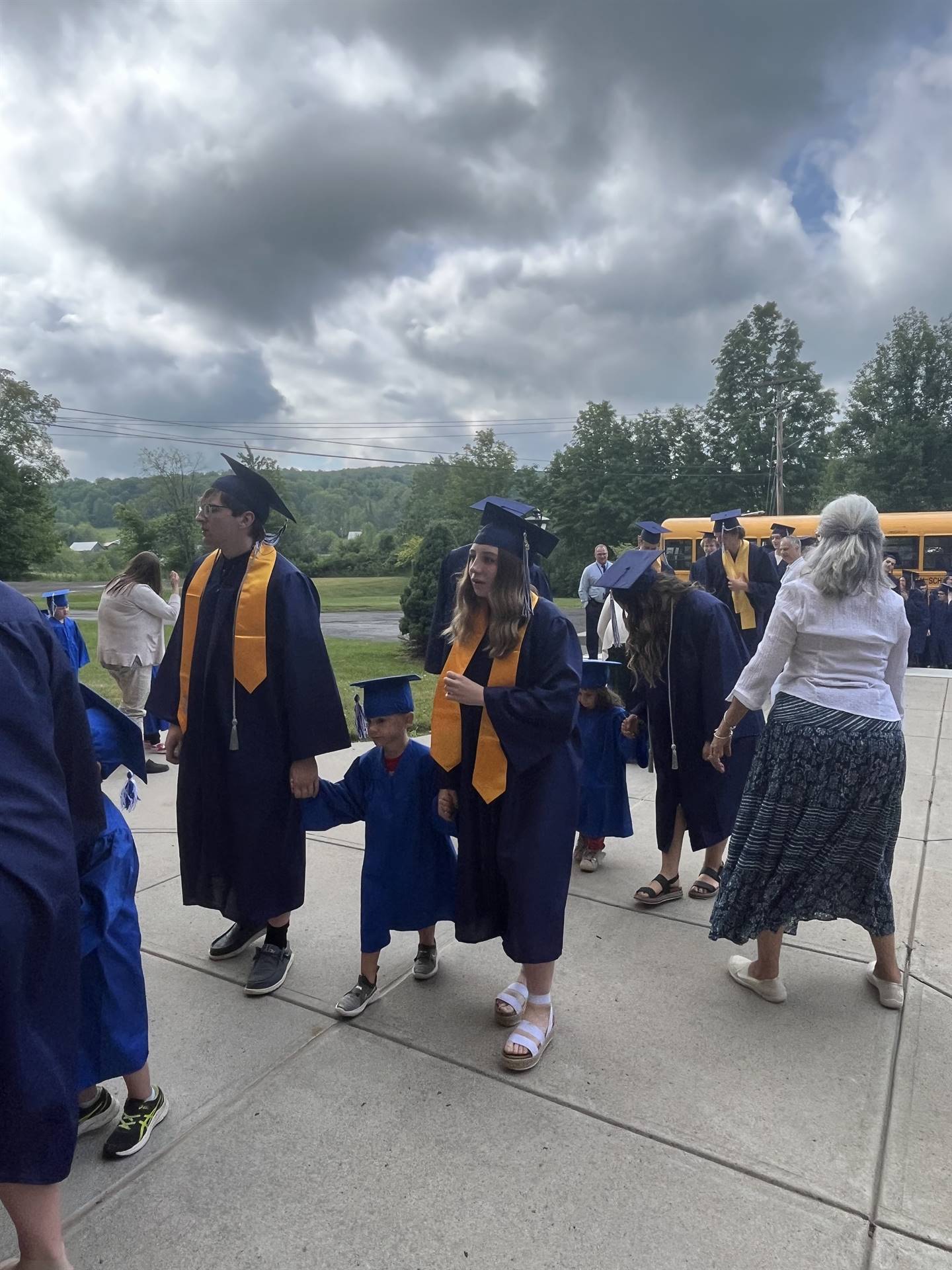 2 2023 senior graduates with a pre k student in middle dressed in caps and gowns