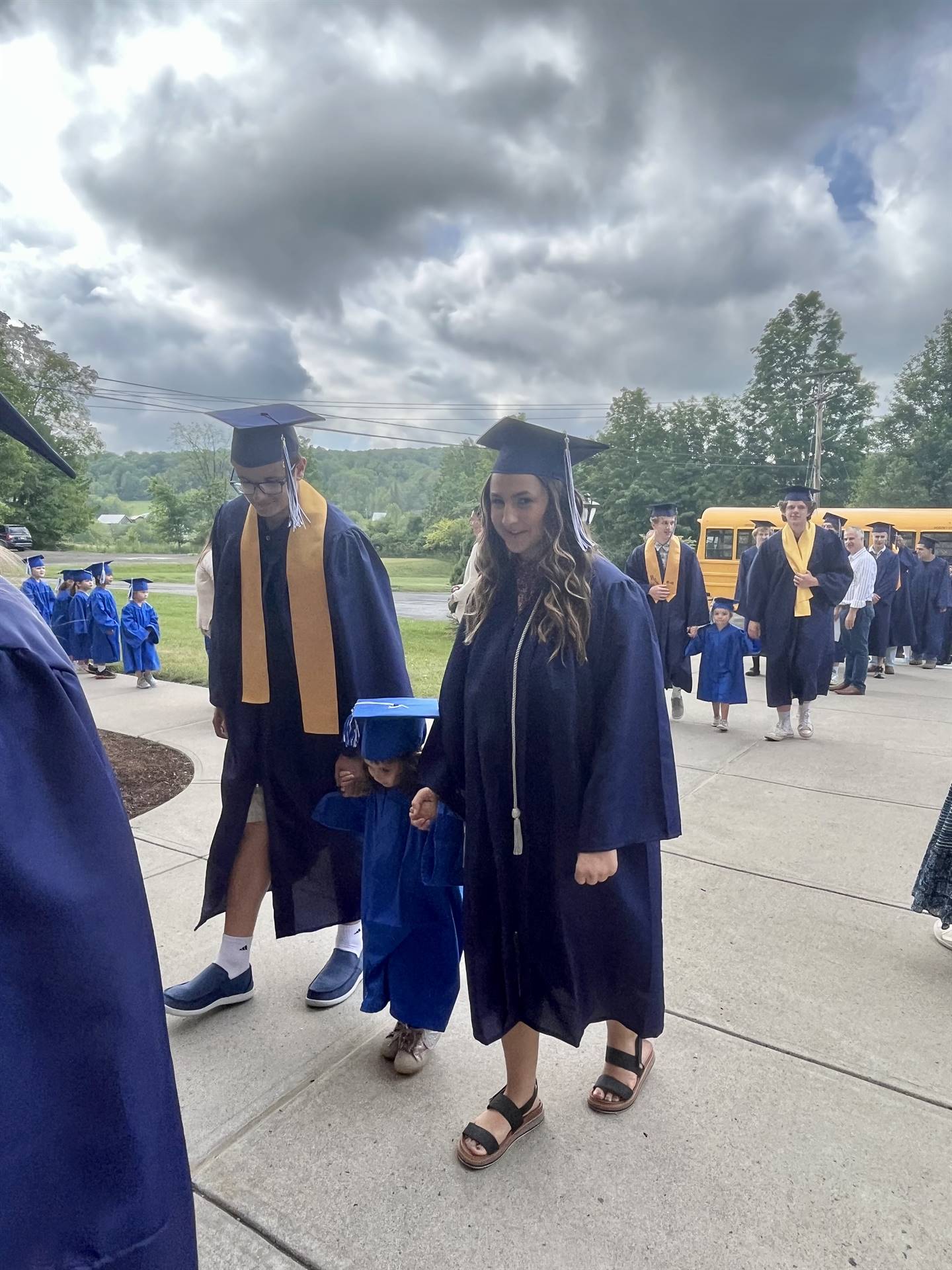 2 2023 senior graduates with a pre k student in middle dressed in caps and gowns