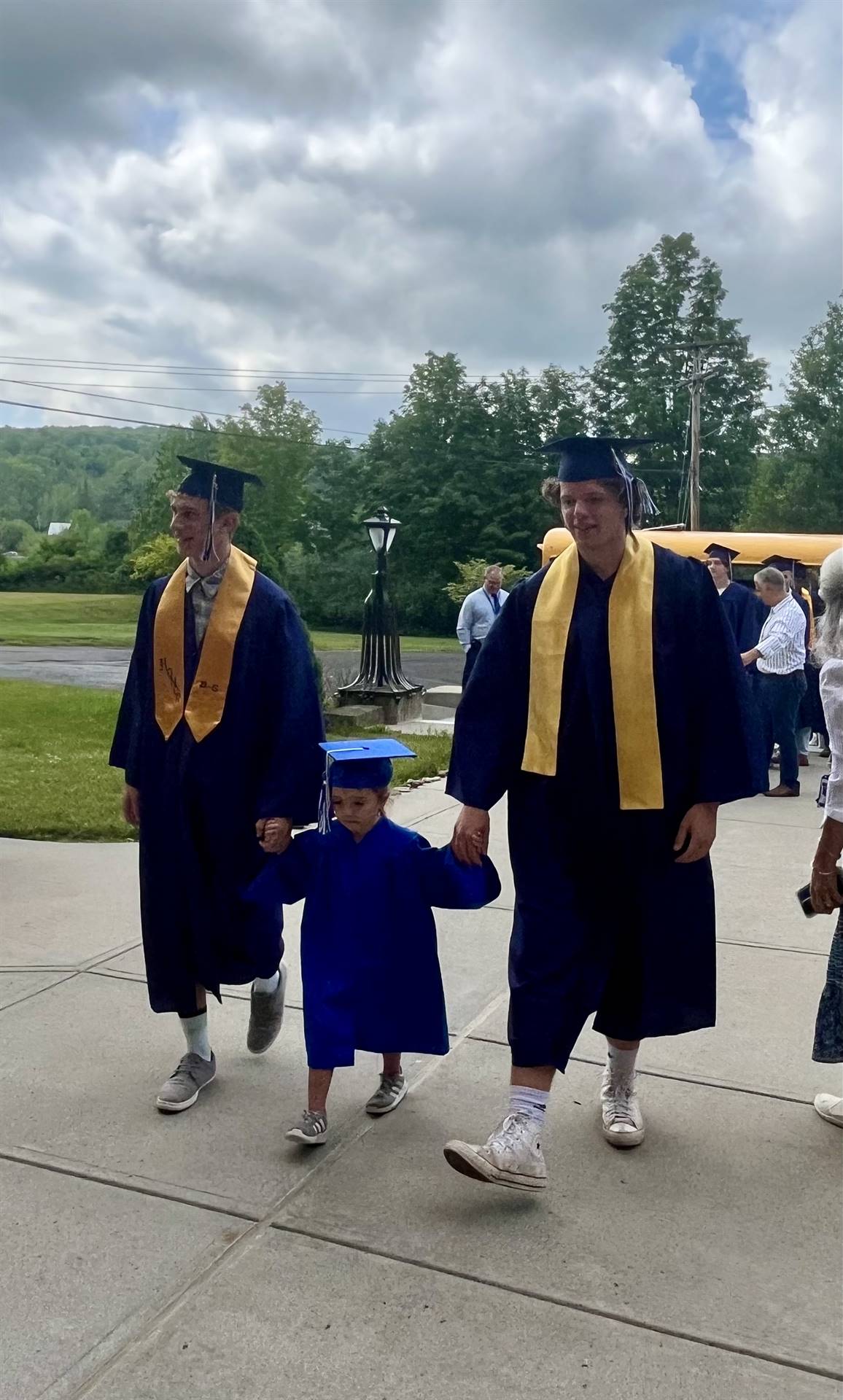 2 2023 senior graduates with a pre k student in middle dressed in caps and gowns