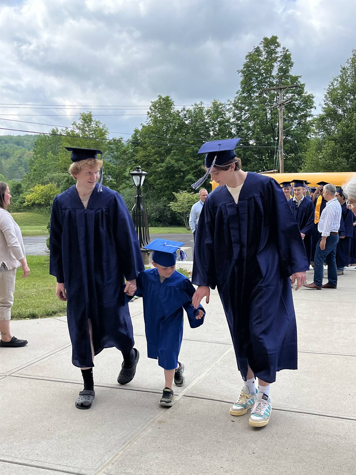 2 2023 senior graduates with a pre k student in middle dressed in caps and gowns