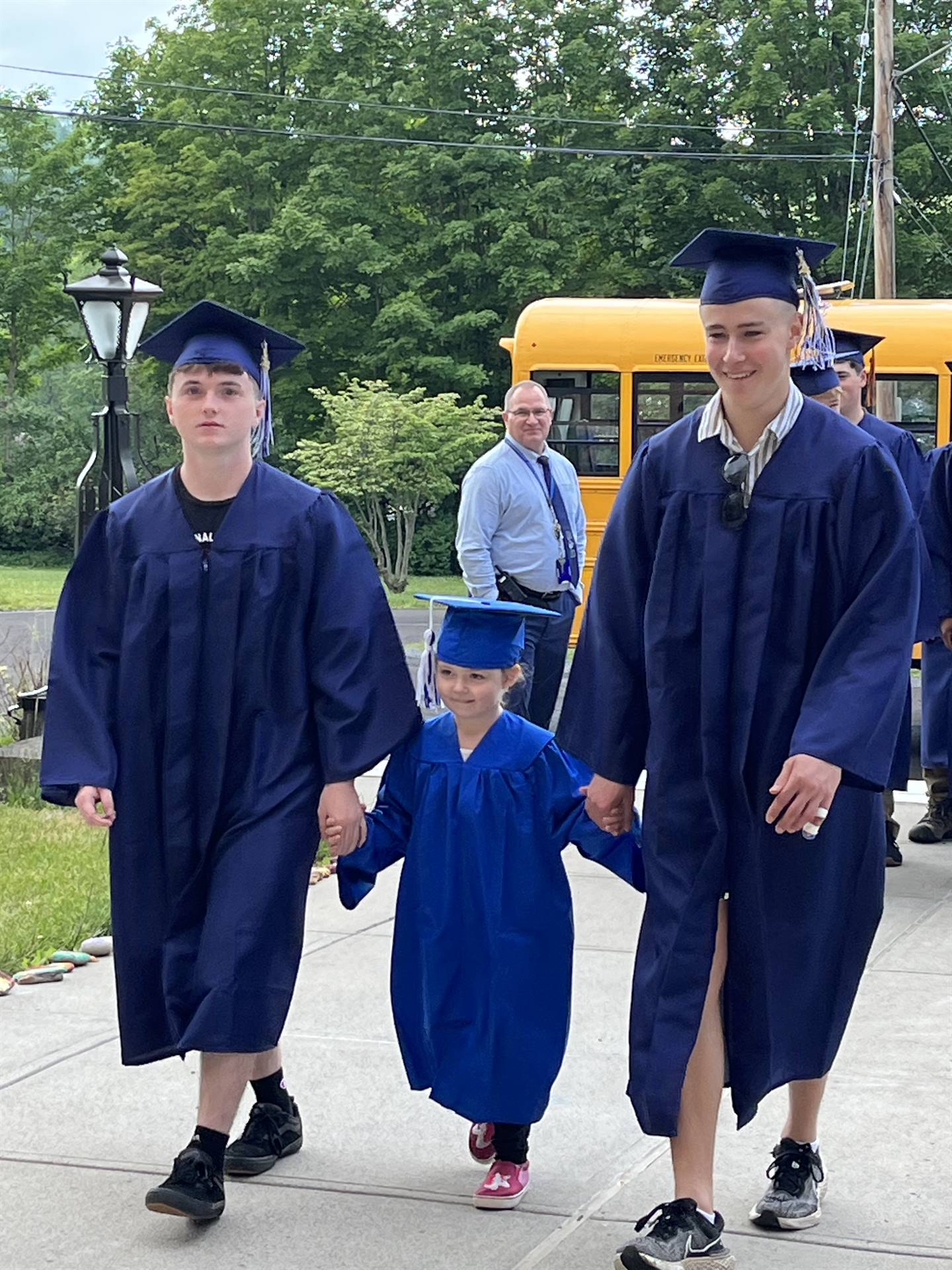 2 2023 senior graduates with a pre k student in middle dressed in caps and gowns