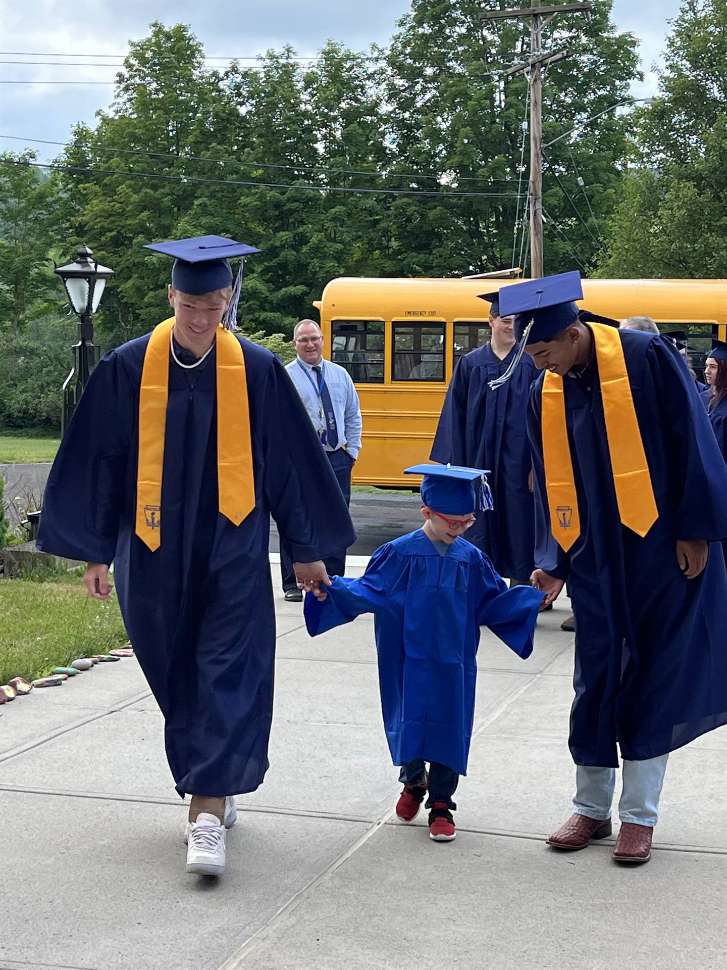 2 2023 senior graduates with a pre k student in middle dressed in caps and gowns