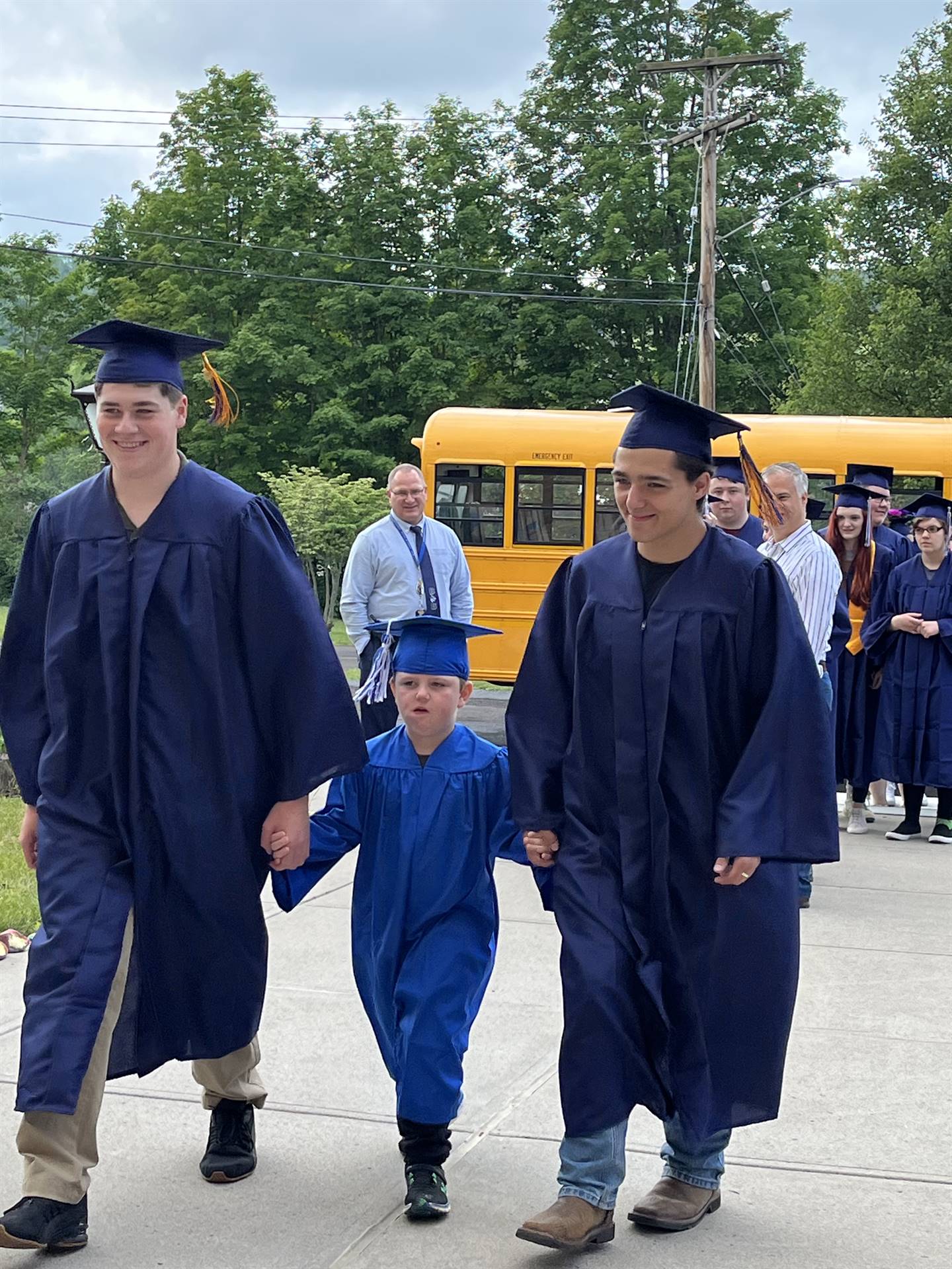 2 2023 senior graduates with a pre k student in middle dressed in caps and gowns