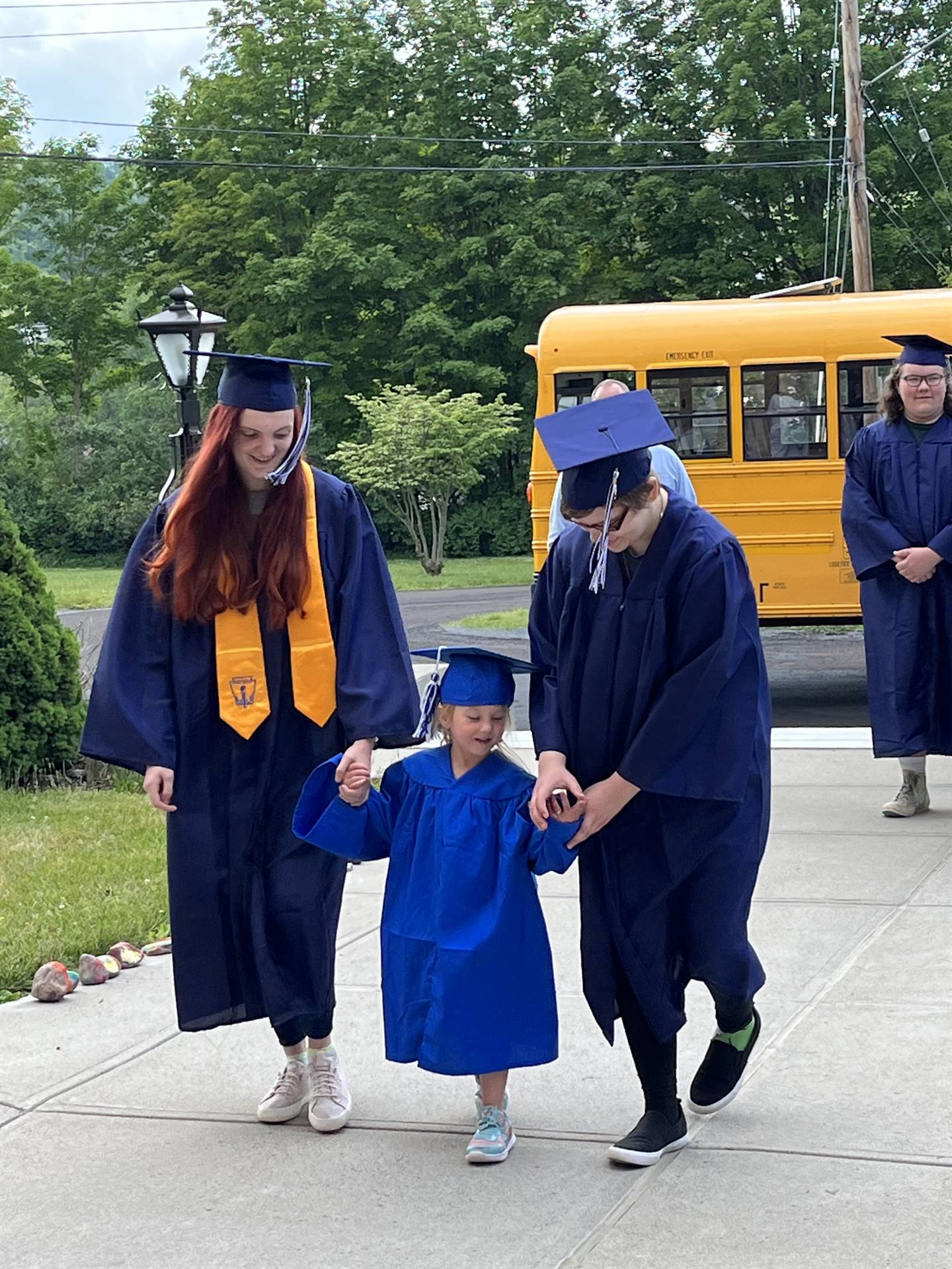 2 2023 senior graduates with a pre k student in middle dressed in caps and gowns