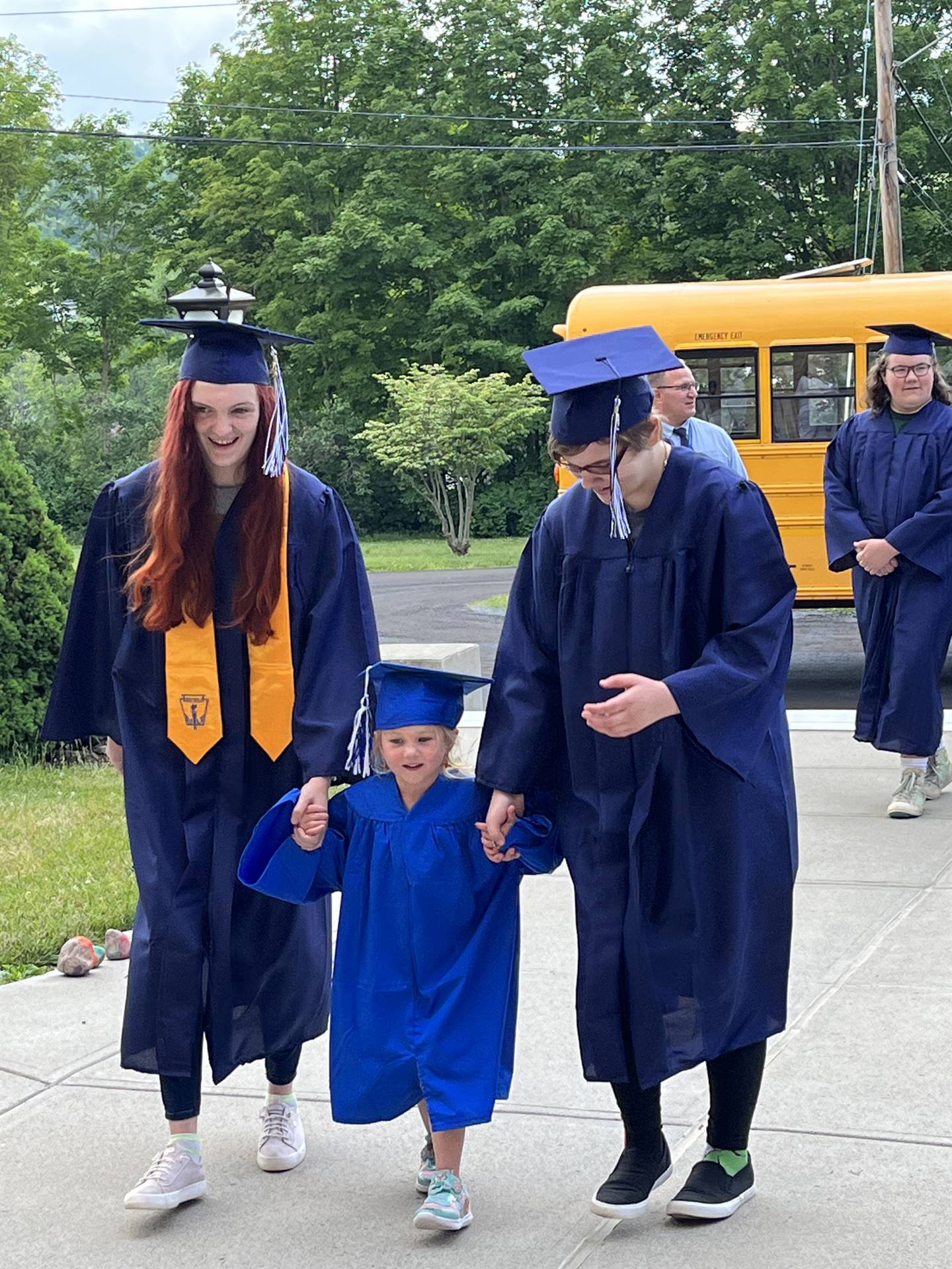 2 2023 senior graduates with a pre k student in middle dressed in caps and gowns